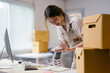© PaeGAG - Young business owner is calculating expenses and managing her online orders from her home office. She is surrounded by cardboard boxes