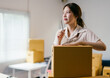 © PaeGAG - Young entrepreneur is holding a pen and thinking about her next business strategy while standing among cardboard boxes