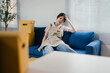 © PaeGAG - Tired woman takes a break on the couch after moving into her new apartment, surrounded by furniture and plants in a cozy living room