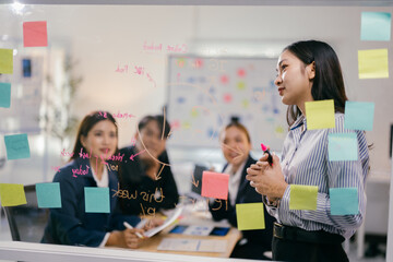 Fototapete - Team of asian businesspeople are having a creative brainstorming meeting in their office conference room, using sticky notes on a glass wall to share ideas