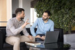 © fizkes - Two business partners discussing work project at laptop, sitting on couch in co-working, talking, meeting for conversation. Company manager, advisor civing consultation to customer