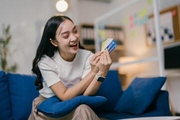 Young woman is sitting on a sofa in her living room, holding a selection of credit cards and laughing. She is happy with her purchase