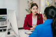 © Parichat - Two businesswomen are sitting at a desk in a modern office, engaged in a serious conversation. The woman in the red blazer is listening intently to her colleague