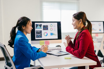 Two businesswomen in a busy office meeting, analyzing financial data on a computer screen, discussing marketing and sales strategies with confidence and teamwork