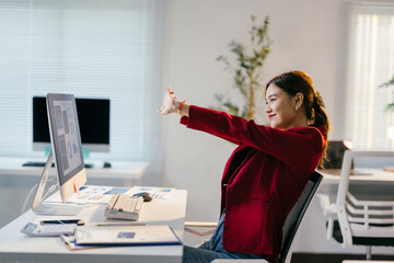 Young businesswoman takes a moment to stretch her arms and relax while working at her computer in her bright, modern office