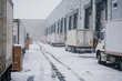 © Degimages - Delivery trucks lined up outside a snow-dusted warehouse, drivers unloading packages in cold