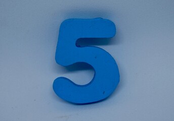 close up photo of a children's toy in the shape of the number five, made of wood and light blue paint