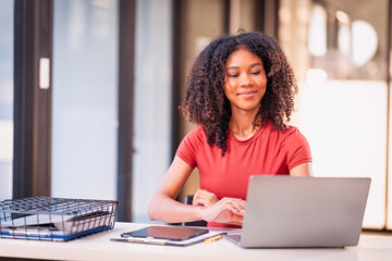 Beautiful professional woman sitting at table smiling while reading important documents with financial graphs and accounting of company.