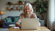 © Ali Hamza Tullah - Happy mature middle aged older woman using laptop computer sitting at table in living room, hybrid working, elearning with technology at home, browsing internet, searching online.