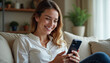 © Ali Hamza Tullah - Smiling relaxed young woman sitting on couch using cell phone technology, happy lady holding smartphone, scrolling, looking at cellphone enjoying doing online ecommerce shopping in mobile apps.