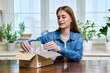 © Valerii Honcharuk - Young female customer sitting at home unpacking cardboard box with online purchases