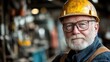 © imagineRbc - A man wearing a yellow hard hat and glasses is standing in a workshop. He looks serious and focused