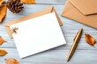 © vilaiporn - A blank greeting card with a golden pen, pine cone, and autumn leaves on a wood surface for seasonal inspiration.