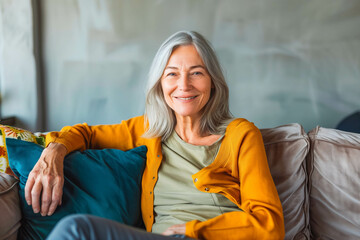 Happy beautiful relaxed mature older adult grey-haired woman relaxing on sofa at home. Smiling stylish middle aged 60s lady enjoying resting sitting on couch in modern living room, with copy space.