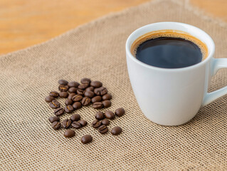 Cup of coffee with heart shape smoke and coffee beans on burlap sack on old wooden background