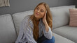 © Krakenimages.com - Woman sitting on a sofa in a living room, smiling with a relaxed expression, wearing a striped shirt, blonde hair cascading over her shoulder, creating a cozy indoor atmosphere.