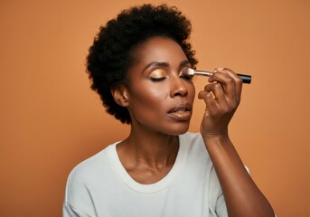 Wall Mural - Beautiful black model with short curly hair is applying eyeshadow makeup on a brown background