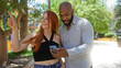 © Krakenimages.com - Interracial couple in an urban park checking directions on a smartphone, with the woman pointing excitedly ahead in a sunny outdoor setting.