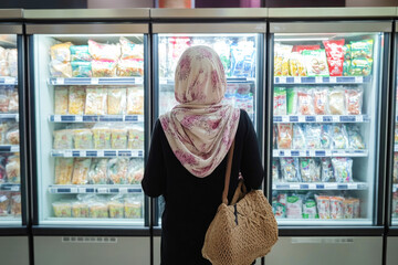 Wall Mural - Woman in hijab shopping at supermarket frozen food aisle with eco-friendly bag