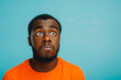 © MVProductions - Portrait of a confused puzzled minded African American man in orange top isolated on blue background, with copy space