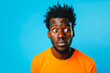 © MVProductions - Portrait of a confused puzzled minded African American man in orange top isolated on blue background, with copy space