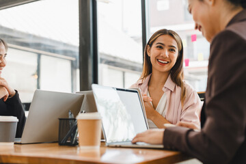 Wall Mural - young woman smiles while engaging in conversation with colleagues at modern office setting. atmosphere is collaborative and friendly, with laptops and coffee cups on table