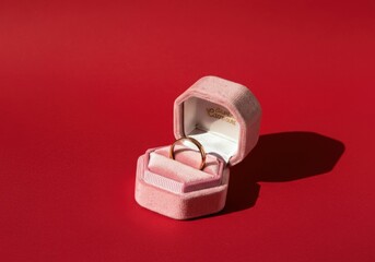 Golden ring sitting in open pink velvet silk box on red background for valentine's day