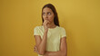 © Krakenimages.com - Young woman standing over isolated yellow background looking concerned with hand on chin wearing yellow t-shirt with wavy brown hair