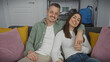 © Krakenimages.com - A smiling couple sits closely on a sofa in their modern living room, portraying affection and comfort.