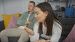 © Krakenimages.com - A woman gestures while talking to a man sitting on a sofa in a modern living room, displaying emotions and communication.