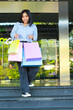 © M Alfan Setyawan - vertical shoot of happy asian woman holding shopping bag smiling feels satisfied while walking in outdoors around mall building