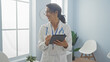 © Krakenimages.com - Smiling hispanic female doctor with stethoscope using tablet in bright clinic office interior.