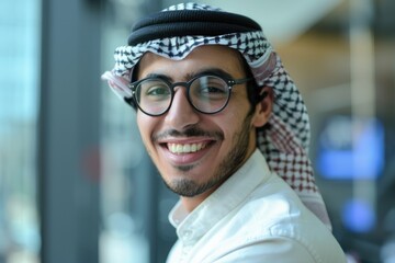 Smiling man wearing traditional Middle Eastern attire in office setting. Attractive business man looking and staring at camera while sitting with blurring background. Happy Business portrait. AIG51.