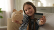 © Yuliia - Happy little girl show at camera piggy bank credit debit card banking money finance smiling budget cash shopping saving calculating capital currency pay transaction child female kid daughter economy