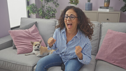 Sticker - Excited woman cheering on couch with a chihuahua watching tv at home.