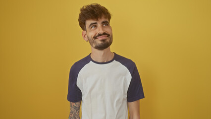 Sticker - A young hispanic man with a beard smiles casually against an isolated yellow background, exuding a relaxed, handsome vibe.