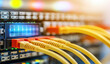 © The Pixel Store - closeup of an internet cable being connected the end port on one side and a network switch with blue wires connected in between on top of it is a colorful display panel showing data flow, Ai