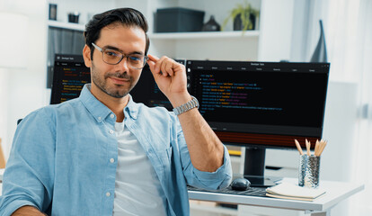 Profile's smart IT developer looking camera to pose wearing glasses against on software development coding on two pc screen, presenting program update online website data at modern office. Surmise.