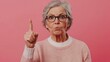 © Grace - Angry Senior Woman With Grey Hair and Glasses Pointing Finger in a Strict Manner Over a Pink Background. Generative AI