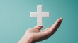 © JK_kyoto - Hand holding a white cross symbol against a turquoise background.