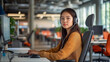 © whoopwhoops - Asian woman with headphone on front of computer, customer service work while sitting at an adjustable desk in a modern office