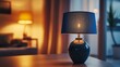 © VINA - A blue lamp with a fabric shade sits on a table in a living room, providing warm light for a cozy evening.