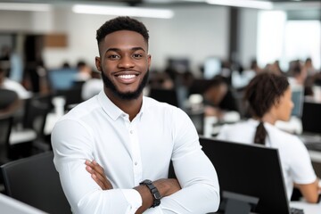 A young man with a bright smile exudes confidence as he poses in an open-plan office, representing professionalism and positivity in a modern work environment.