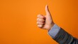 © MAGIC  FHOTOS - A hand with a raised finger signaling approval against a bright orange background, symbolizing a positive affirmation