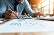© Odin AI - Close-up of hands using a pen to analyze graphs on paper, signifying detailed financial market analysis and professional work in contemporary economic research.