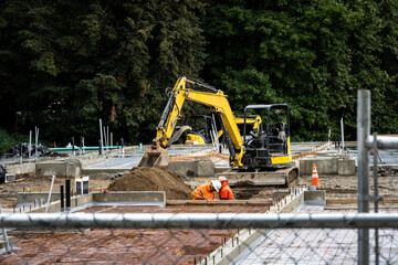 New construction started in a mixed use commercial and industrial zone, cleared job site with foundation started, heavy equipment and workers behind chain-link fence
