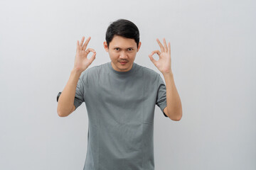 Happy expression of adult Asian man doing OK sign with casual t-shirt isolated on white background