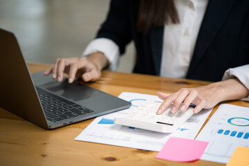 Close up of hands typing on laptop keyboard and working on document paperwork and calculator for cost financial marketing