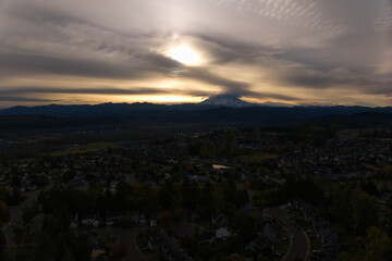 Mount Rainier during a cloudy sunrise, aerial view of suburban homes and dramatic skies in Washington State, USA