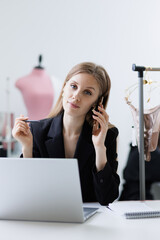 Wall Mural - Online purchase of craft underwear from seamstress tailor. Young woman salesperson is talking on phone and working on laptop